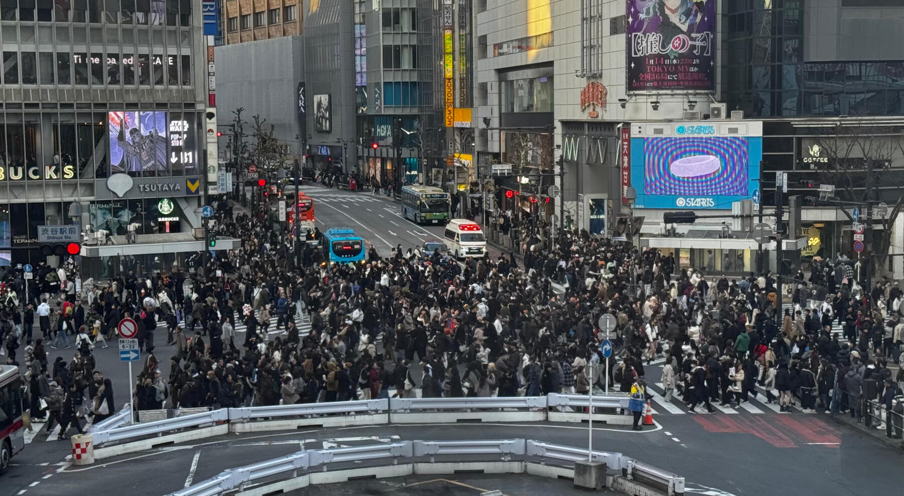 Crowds crossing a busy city intersection from above