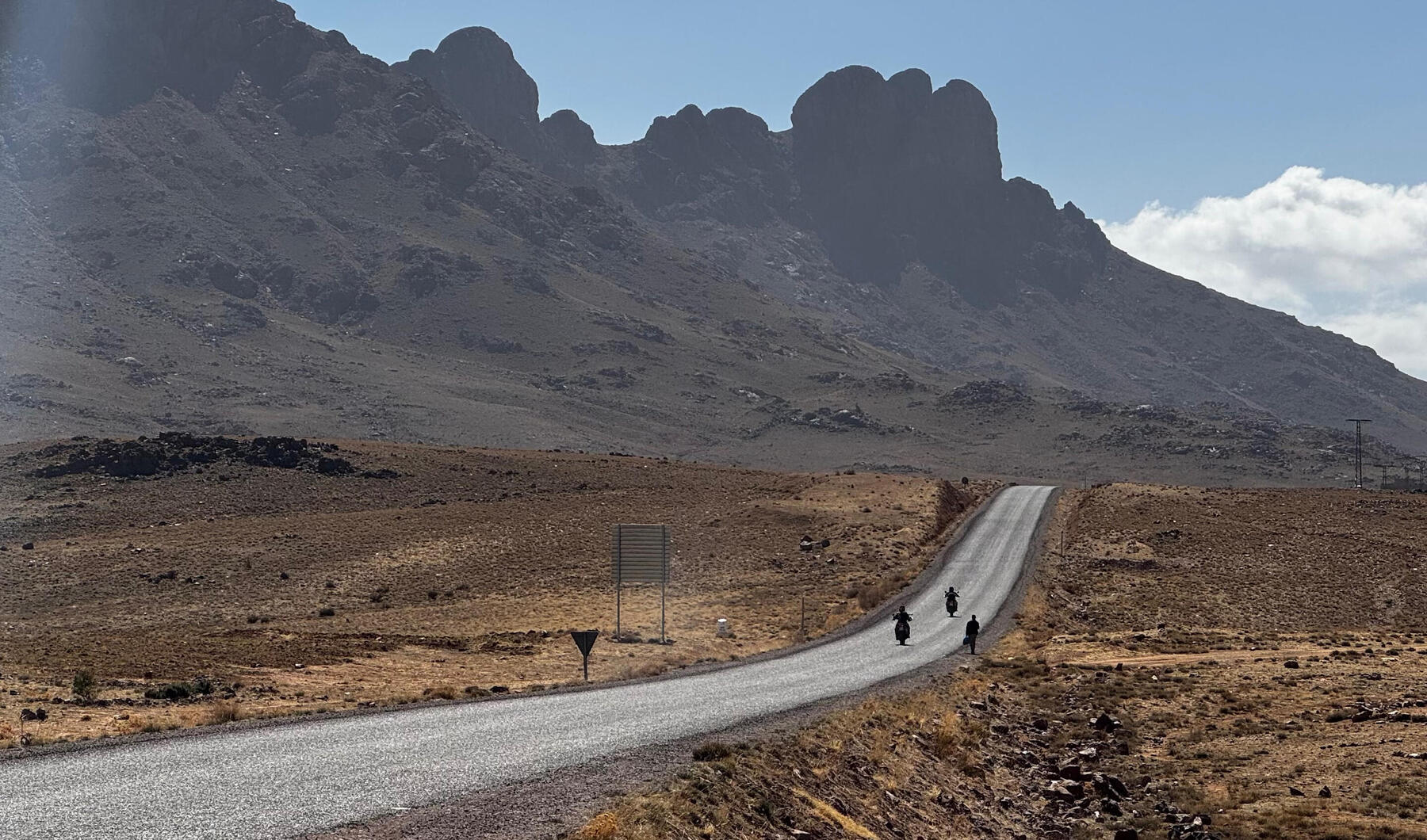 Two motorbikes on an empty road toward a rocky mountain range
